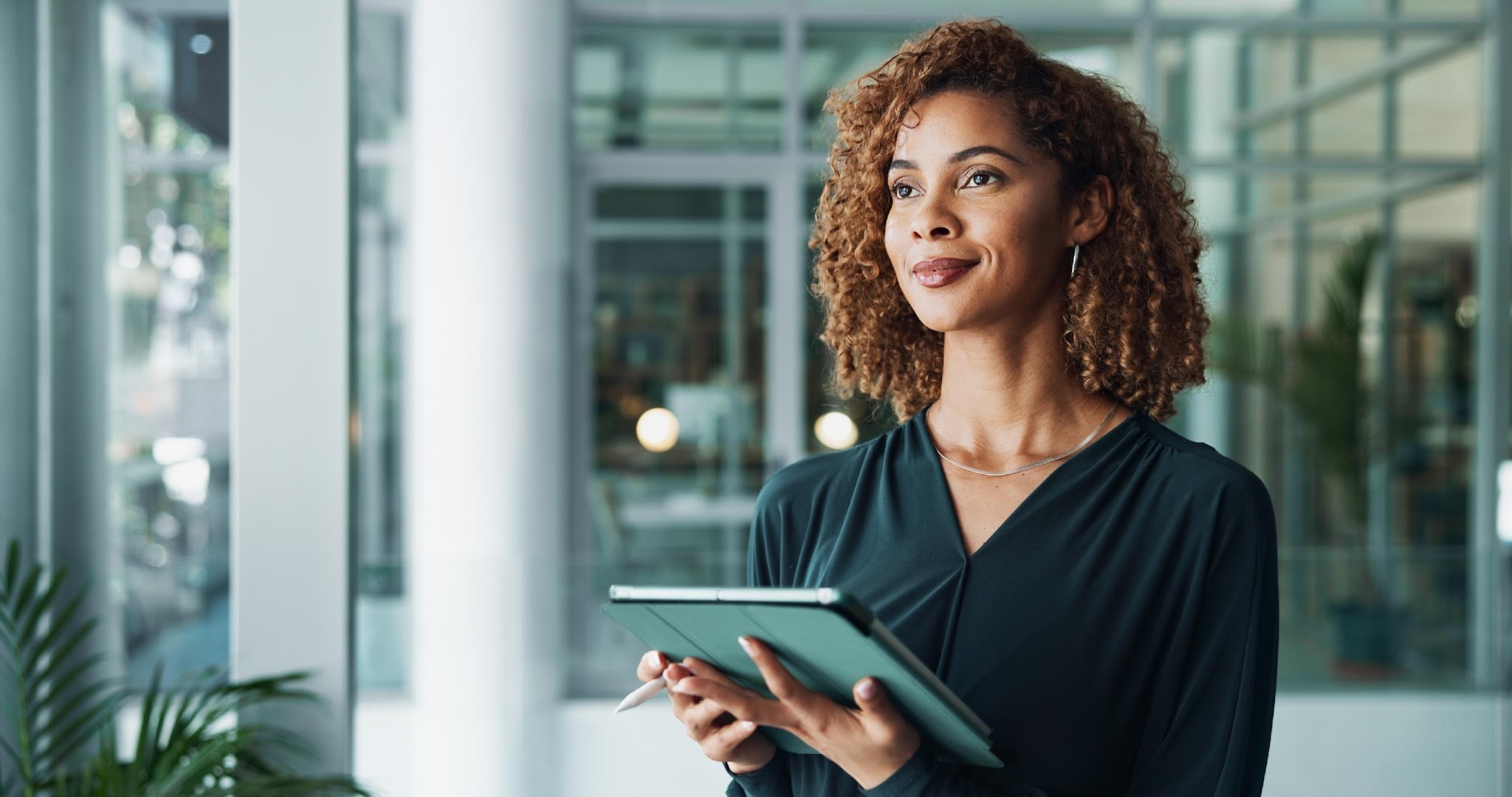 Confident professional woman holding a tablet in a modern glass office